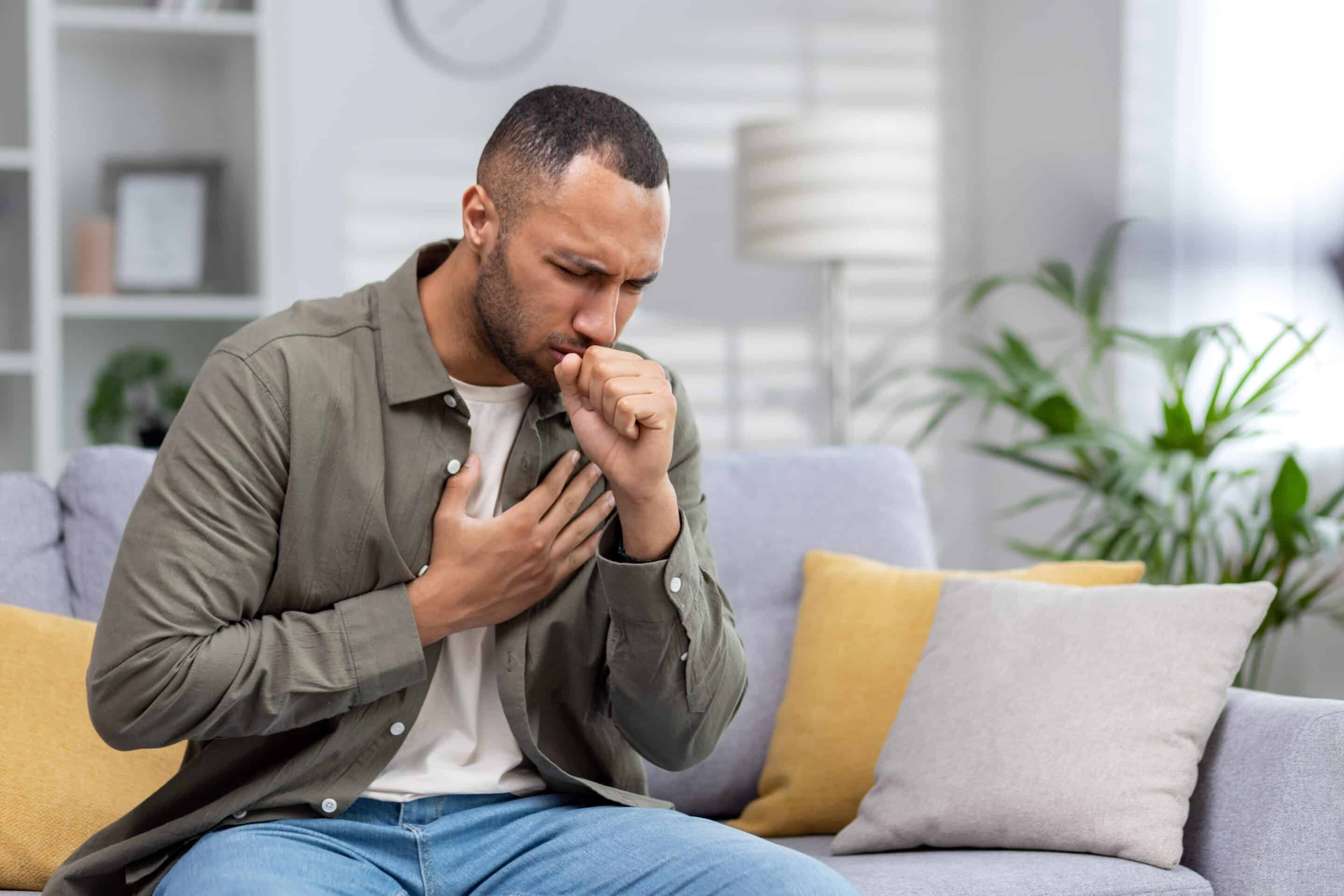 Man sitting on the couch at home and coughing.